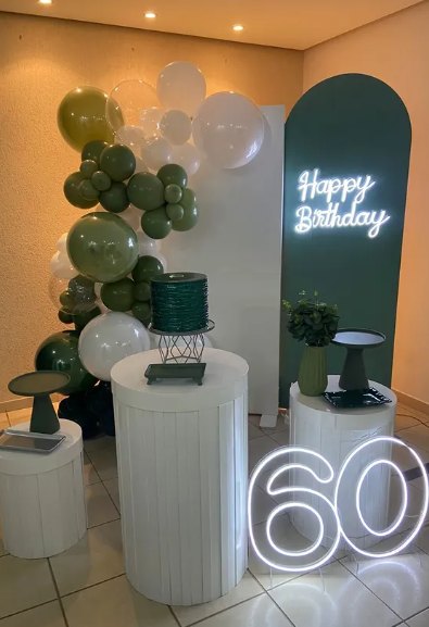 Cenário de 60 anos com arco de balões verde-oliva, painel em arco verde e letreiro de neon Happy Birthday